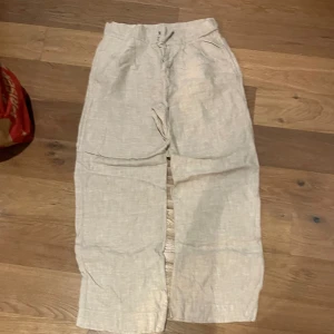 Beiga linnebyxor med snörning - Snygga och luftiga beiga linnebyxor med avslappnad passform och snörning i midjan. Perfekta för varma dagar och chill stunder. Byxorna har raka ben och sidofickor för en enkel och clean look.