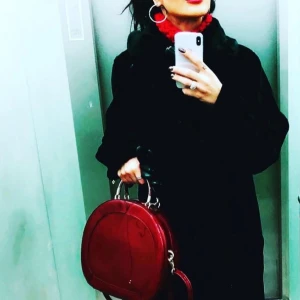 Röd rund handväska i skinn - Säljer en riktigt snygg rund handväska i blankt rött skinn. Väskan har två handtag och en axelrem, perfekt för dig som vill sticka ut med en unik form. Stängs med dragkedja och har en stilren look som passar till många outfits. Handskar i bilden ingår inte