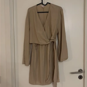 Beige omlottklänning från H&M Mama - Snygg beige omlottklänning från H&M Mama i storlek S. Klänningen har lång ärm, v-ringning och knytband i midjan för en skön passform. Aldrig använd. 