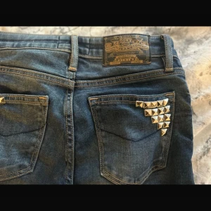 Crocker blå jeans med spets och nitar - Snygga blå jeans från Crocker med bootcut passform. Dekorerade med silvriga nitar på bakfickan och mörkblå spetsdetaljer längs benen☺️