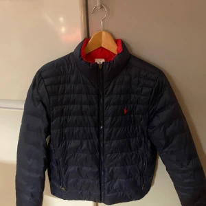 Dunjacka polo Ralph lauren  - En riktig skön och lätt dunjacka nu for vintern. Man kan även väckla ut jackan så att den blir röd ifall man skulle vilja göra det. Storlek: Barn XL (18–20), motsvarar ca 164–170 cl / 14–16 år.