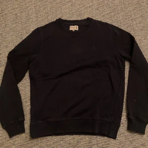 Morris - Svart sweatshirt från Morris i storlek S. Tröjan har rund hals, långa ärmar och ett diskret broderat emblem på bröstet. Tillverkad i mjuk bomull med ribbade muddar vid ärmslut och nederkant. Perfekt för chill dagar och enkel att matcha.