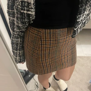 Rutig brun minikjol i ullmix - Superfin rutig minikjol i bruna och blå toner. Kjolen har klassiskt rutmönster och är sydd i en mjuk ullmix som känns både trendig och tidlös. Perfekt att styla med boots eller sneakers för en cool look.