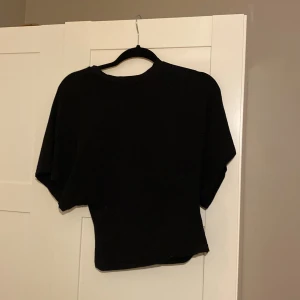 Svart topp från Nelly  - En svart topp från Nelly i storlek XS. Lite bredare armar och toppen går in i midjan. 