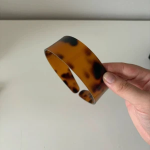 Bred diadem i sköldpaddsmönster - Snyggt och brett diadem i klassiskt sköldpaddsmönster med bruna och svarta toner. Tillverkat i blank plast med rundad form som sitter bekvämt på huvudet. Perfekt accessoar för att lyfta din look och hålla håret på plats. Carolyn Bessette inspirerarad stil 