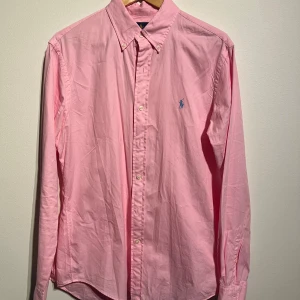 Ralph Lauren rosa skjorta, storlek L - Rosa skjorta med en broderad logotyp på bröstet. Skjortan har en button-down krage.  Skick: Mycket gott skick, sparsamt använd utan defekter.  Storlek: M men sitter absolut inte som en M utan som en L  Kolla gärna in mina andra annonser.   Skriv vid frågor eller ifall du vill ha fler bilder. 