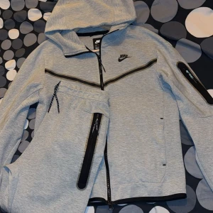 Grå Nike tech dress - Säljer den pga att den har blivit för liten på mig annars är den fin och bekväm. Storlek S på både byxorna och tröjan.