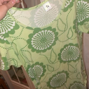 Grön blommig kortklänning från Monki - Superfin ljusgrön T-shirt från Monki med stora gröna och vita blommor. T-shirten har rund halsringning och korta ärmar. Perfekt för dig som gillar färg och mönster! Materialet är mjukt och skönt, troligtvis bomull.