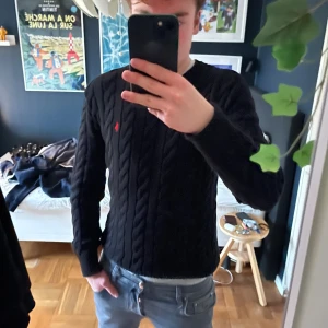 Svart kabelstickad tröja Polo Ralph Lauren - Svart kabelstickad tröja från Polo Ralph Lauren med klassisk röd logga broderad på bröstet. Rund hals och ribbade muddar vid ärmslut och nederkant. Tillverkad i mjuk premium bomull. Storlek S men stor i storleken så kan även passa M. Äkta! Fråga gärna angående qr kod eller storlek!🍾👌