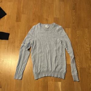 Ljusgrå ulltröja från NN07 - Snygg ljusgrå långärmad tröja från NN07, modell Ted, tillverkad i 100% mjuk ull med italianskt garn. Tröjan har en klassisk rund hals och ribbade muddar vid ärmslut och nederkant. Perfekt för dig som gillar stilrena och bekväma plagg. Nypris 1300