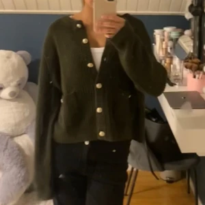 Hm kofta - Säljer en mörkgrön, croppad kofta med stora guldknappar och två fickor framtill. Koftan är stickad och har långa ärmar, perfekt för lager-på-lager och chill vibes. Snygg att styla med både jeans och kjol.