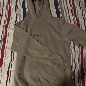 Beige hoodie från Mennace XS - Säljer en beige hoodie från Mennace i storlek XS. Tröjan har en stilren design med svart logotyp på bröstet, huva och klassisk känguruficka. Materialet är en skön mix av bomull och polyester, perfekt för chill dagar. Passformen är normal och ärmarna är långa.