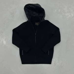 Apex cardigan från Leon Marcel - Svart cardigan från Leon Marcél. Tröjan har dragkedja framtill och två sidofickor med dragkedja. Passformen är normal och materialet känns rejält och mjukt. Perfekt för dig som gillar stilren och enkel design.