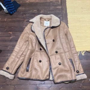 Beige pälsjacka med knappar - Säljer en beige pälsjacka med dubbla rader svarta knappar och mysigt foder. Jackan har detaljer i mörkbrunt vid fickor och kanter samt bred krage och uppvikta ärmslut. Perfekt för kalla dagar och riktigt snygg till jeans eller boots.