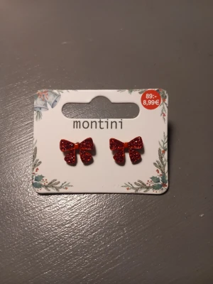 Röd glittrig rosettörhängen Montini(Ur och pen) - Säljer ett par superfina örhängen från Montini(Ur och pen) i form av röda rosetter med glitter. Perfekta för att ge din look lite extra bling! Fäste i metall och snygg detalj till jul eller fest. Andning andvänd.