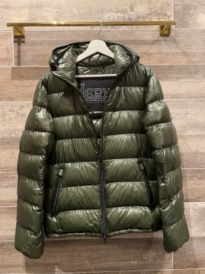 Herno jacka  - Säljer en olivgrön pufferjacka från Herno med glansig finish och huva. Jackan har dragkedja framtill och två snedställda fickor med dragkedja. Perfekt för kalla dagar och riktigt lätt att bära. Klassisk quiltad design och stilren look. Size 50 passar M. Typ helt ny