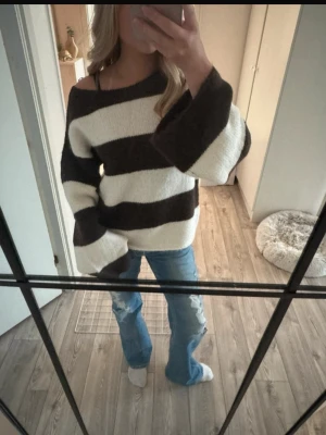 Randig stickad tröja med vida ärmar - Säljer en mysig stickad tröja med breda bruna och vita ränder. Tröjan har en loose passform, vida långärmar och en något offshoulder halsringning. Perfekt för chill dagar och enkel att styla med jeans eller leggings. Storlek 158/164 men är stor i storleken och passar S