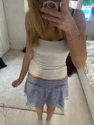 Ljusblå blommig volangkjol - Supersöt ljusblå kortkjol med små blommor och volangdetaljer. Kjolen har resår i midjan och är gjord i ett tunt, flowy material som känns luftigt och perfekt för varma dagar. Inga defekter. Hör av er för fler frågor💗💗