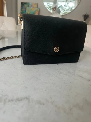 Svart axelväska från Tory Burch - Snygg svart axelväska från Tory Burch med guldfärgade detaljer och kedja. Väskan har en defekt, se sista bild men inget man märker av❤️