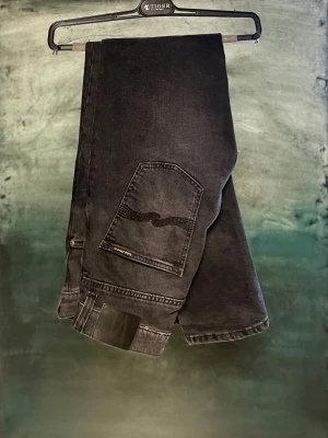 Nudie Jeans herr - Säljer ett par svarta jeans från Nudie Jeans Co med klassisk femficksdesign och diskret logga på bakfickan. Jeansen har en slim fit passform och är tillverkade i slitstarkt bomullsmaterial. Snygg tvättad look och perfekta till sneakers eller boots.