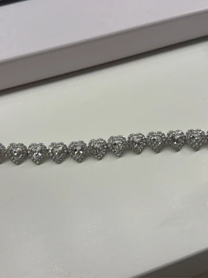 Ariana Grande x Swarovski armband - Supersnyggt armband från Ariana Grande x Swarovski med hjärtformade, gnistrande stenar i vitt. Armbandet är rhodiumpläterat och har en exklusiv känsla med sina glittriga detaljer. Perfekt accessoar för att lyfta vilken outfit som helst. Helt ny