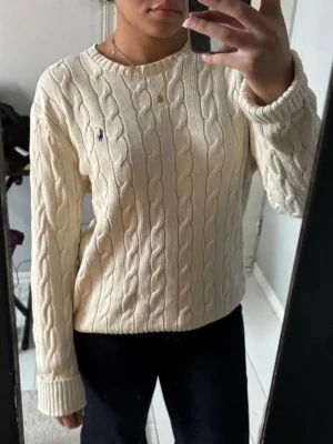 Stickad tröja från Ralph Lauren - Stickad cremevit tröja från Ralph Lauren med klassisk blå logga broderad på bröstet.🩷Tröjan har rund halsringning, långa ärmar och ribbade muddar.🩷