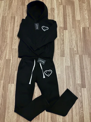 Carsicko tracksuit  - Svarta mjukisbyxor från Carricko med vit snörning i midjan och ett broderat hjärta med ansikte på vänster lår. Byxorna har en loose passform och är gjorda i mjukt bomullsmaterial, perfekta för chill dagar. Snygg kontrast med vita detaljer. Aldrig använd nytt skick. Varm och skön 