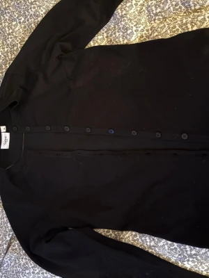 Svart kofta från Saint Tropez - Svart klassisk kofta från Saint Tropez med rund hals och knappar hela vägen framtill. Långärmad och tillverkad i mjuk bomull, perfekt att slänga över en t-shirt eller linne. Enkel och stilren design som funkar till många olika looks.