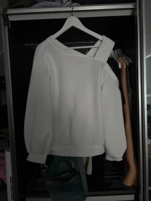 Vit sweatshirt från Ellemilla - Säljer en vit långärmad tröja från Ellemilla med unik omlottdetalj vid halsen. Tröjan har en loose passform och är tillverkad i mjukt syntetmaterial. 