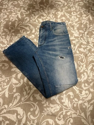 Patchade blå jeans från Jack & Jones - Säljer ett par blå jeans från Jack & Jones med coola patchade detaljer och slitningar på benen. Modellen är Travis Original och har klassisk femficksdesign. Jeansen har normal passform och är tillverkade i bomull. Perfekt för dig som gillar en unik streetstil.