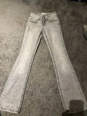 Grå bootcut jeans från Gina tricot   - Snygga grå jeans från  Gina Tricot  med bootcut-snitt och klassisk femficksdesign. Baktill finns fickor med knapp detalj. Jeansen har en ljusgrå tvätt och är tillverkade i mjukt denim-material. Perfekt för dig som gillar en avslappnad men stilren look.