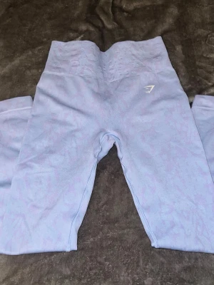 Ljuslila seamless leggings från Gymshark - Supersnygga ljuslila seamless leggings från Gymshark med hög midja och diskret mönster. Stretchigt material som sitter tight och formar sig efter kroppen. Perfekta för gymmet eller andra träningspass. Gymshark-logga på låret.