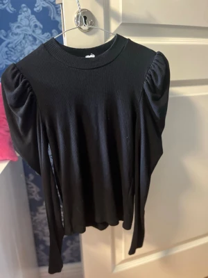 Svart ribbad långärmad topp - Säljer en svart ribbad topp med puffade axlar och lång ärm. Toppen har rund halsringning och är tillverkad i ett mjukt, stretchigt material som sitter snyggt på kroppen. Perfekt för dig som gillar stilrena och trendiga plagg. Från Gina Tricot Dock finns inte lappen kvar. Storlek S men stretchigt material så passar större storlekar. 