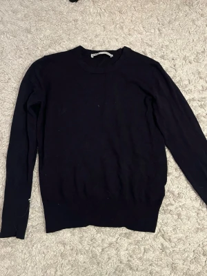 Mörkblå stickad tröja från Zara - Mörkblå stickad tröja från Zara i storlek M. Tröjan har rund halsringning och långa ärmar med snygga guldfärgade knappar vid ärmsluten.