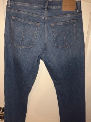 Blå jeans från Tiger of Sweden 32/32 - Säljer ett par klassiska blå jeans från Tiger of Sweden i modellen Marty. Jeansen har fem fickor, knapp och dragkedja fram samt snygga kontrastsömmar. Materialet är slitstark bomull och passformen är rak och normal.