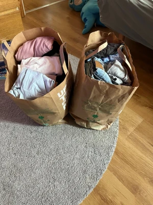 2 påsar med kläder  - Säljer 2 påsar med kläder i påsarna finns det Tröjor, T-shirt, Linnen, Kjolar, Klänningar, Byxor och Shorts. På bilden där de är 4 bilder där är de bilder på alla kläder som finns i påsarna och bilden med ett papper står alla storlekar.