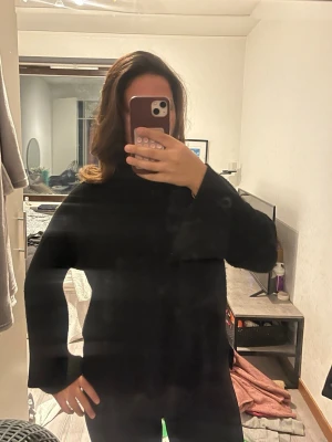 Svart ribbad stickad tröja - En svart stickad tröja med ribbad struktur och lång ärm. Tröjan har en enkel och clean design med rak passform och hög hals. Perfekt att styla med jeans eller kjol för en chill look.