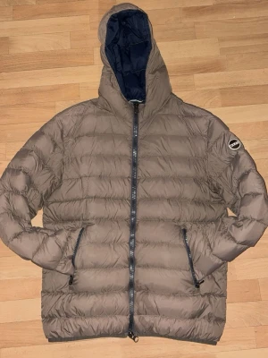 Brun/beige dunjacka från Colmar med huva - Säljer en brun dunjacka från Colmar med huva.En liten fläck vid dragkedjan går bort i tvätten.Storlek S och såklart äkta 