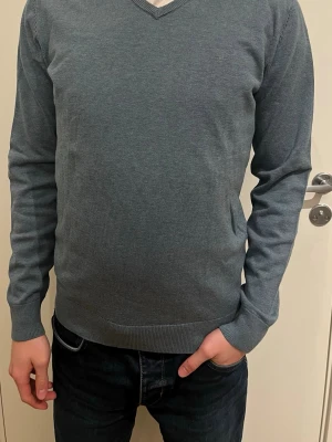 Tröja från Tom Tailor - Snygg ljusblå  tröja från Tom Tailor  med diskret broderad logga på bröstet. Tröjan har v-ringning, ribbade muddar och är långärmad. Perfekt till jeans för en clean och stilren look.