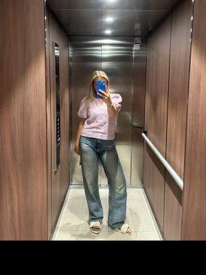 Ljusrosa blus med puffärm från Vila - Supersöt ljusrosa blus från Vila med korta puffärmar och crinklad struktur. Blusen har rund halsringning och är tillverkad i ett lätt, syntetiskt material som ger en cool textur. Perfekt att styla med jeans eller kjol för en trendig look.