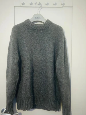 Grå stickad tröja  - Mysig grå stickad tröja från med ribbade muddar vid hals, ärmslut och nederkant. Tröjan har en  Enkel och stilren design som funkar till allt. Perfekt för kyliga dagar.