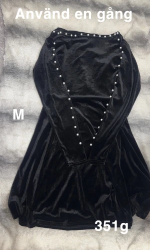 Svart sammetsklänning med pärlor M - Supersnygg svart sammetsklänning med långa ärmar och pärldetaljer längs axlar och ärmar. Klänningen har en mjuk, glansig finish och en klassisk, lite utsvängd form. Perfekt för dig som vill sticka ut med stilrena detaljer.🌸Använd en gång. Storlek M
