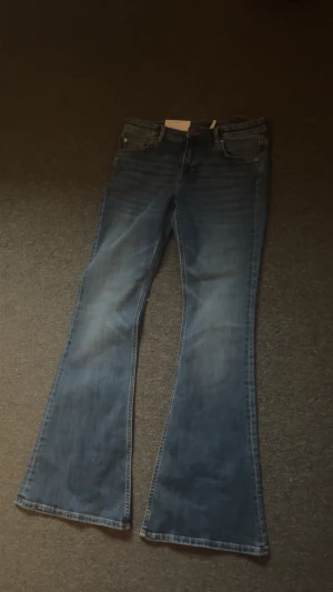 Blå bootcut jeans från Monki w29/32 - Säljer ett par snygga blå jeans från Monki med klassisk bootcut passform. Jeansen har fem fickor, normal midja och är tillverkade i ett slitstarkt denimtyg. Perfekt för dig som gillar retrovibbar och vill ha ett par jeans med lite extra vidd nedtill.