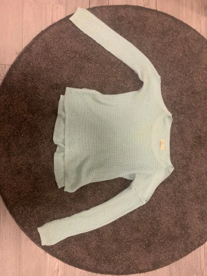 Stickad tröja med bara axlar från Hollister - Säljer en ljusblå stickad tröja från Hollister i storlek xs.Tröjan har långärmade ärmar, rund halsringning och ett snyggt strukturerat stickat mönster. Nederdelen har en liten slits på sidorna för extra detalj. Perfekt för dig som gillar chill och enkel stil.