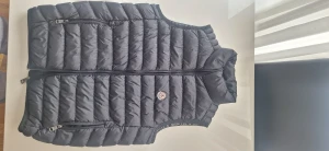 Svart pufferväst från Moncler - Säljer en svart pufferväst från Moncler med quiltad design och logotyp på bröstet. Västen har dragkedja framtill och två sidofickor med dragkedja. Insidan har coolt Moncler-tryck och ser riktigt clean ut. Perfekt för lager-på-lager under höst och vinter.