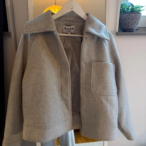 Grå jacka från NA-KD - Säljer en stilren grå overshirt jacka från NA-KD med stor krage och en rejäl ficka framtill. Jackan har dragkedja och tryckknappar, loose fit.