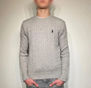 Polo Ralph Lauren Stickad Tröja - Snygg stickad grå tröja från Polo Ralph Lauren i klassisk kabelstickad design. Mjukt och behagligt material som sitter bra på kroppen. Använd en gång och i perfekt fint skick utan defekter. Perfekt för både vardag och mer uppklädda tillfällen
