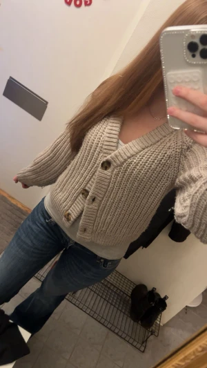 Stickad kofta - Superfin, grovstickad kofta i en varm beige ton. Modellen har en vid v-ringning och stora dekorativa knappar framtill. Passar perfekt både till jeans och klänningar för en mysig men stilren look.😻