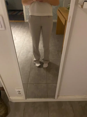 Beige bootcut kostymbyxor Bik Bok - Snygga beige kostymbyxor från Bik Bok i storlek 34. Byxorna har bootcut passform, låg midja och bälteshällor. De är tillverkade i ett mjukt och stilrent material med pressveck och fickdetaljer bak. Perfekta för en clean och trendig look.