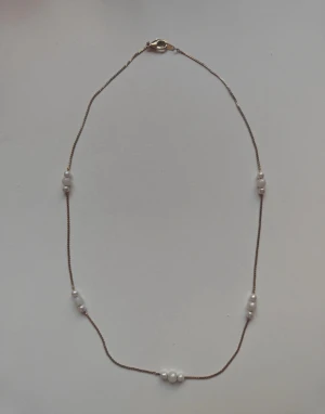 Tunt halsband med vita pärlor - Snyggt och minimalistiskt halsband med tunn kedja i guldton och fem grupper av små vita pärlor. Perfekt för att ge en clean och elegant touch till din outfit. Lätt att matcha med andra smycken och har ett smidigt lås.
